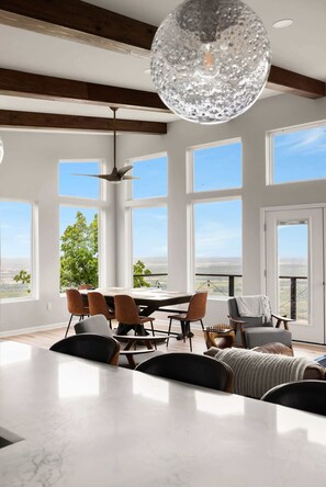 Un'ampia sala da pranzo con un tavolo grande e sedie, ampie finestre che offrono vista sull'esterno e un moderno lampadario.