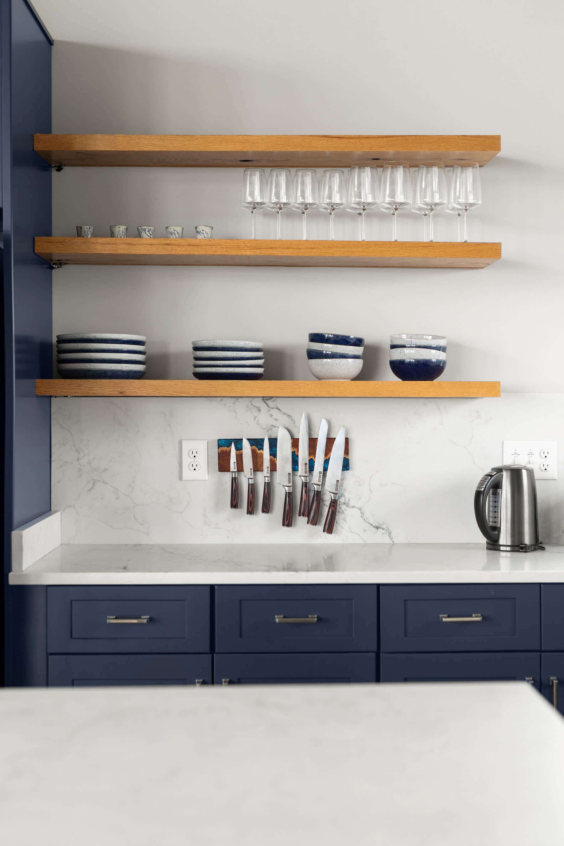 A kitchen with wooden shelves, marble countertops, and blue cabinets.