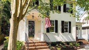 A two-story house with a front porch, a brick staircase, and an American flag.