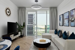 A modern living room with a flat-screen TV, a round coffee table, a sofa, and a large window with a city view. - Urban Parkside Living Near the Iconic Dubai Frame (Dubai)