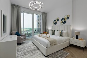 A modern bedroom with a large bed, a desk, a chair, a bedside table, and a view of the outdoors through a large window. - Urban Parkside Living Near the Iconic Dubai Frame (Dubai)
