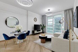 A modern living room with a dining area, a sofa, a TV, and a large window with curtains. - Urban Parkside Living Near the Iconic Dubai Frame (Dubai)