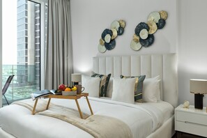 A modern hotel room with a large bed, a bedside table with a lamp, a fruit bowl, and a view of the city through a large window. - Urban Parkside Living Near the Iconic Dubai Frame (Dubai)