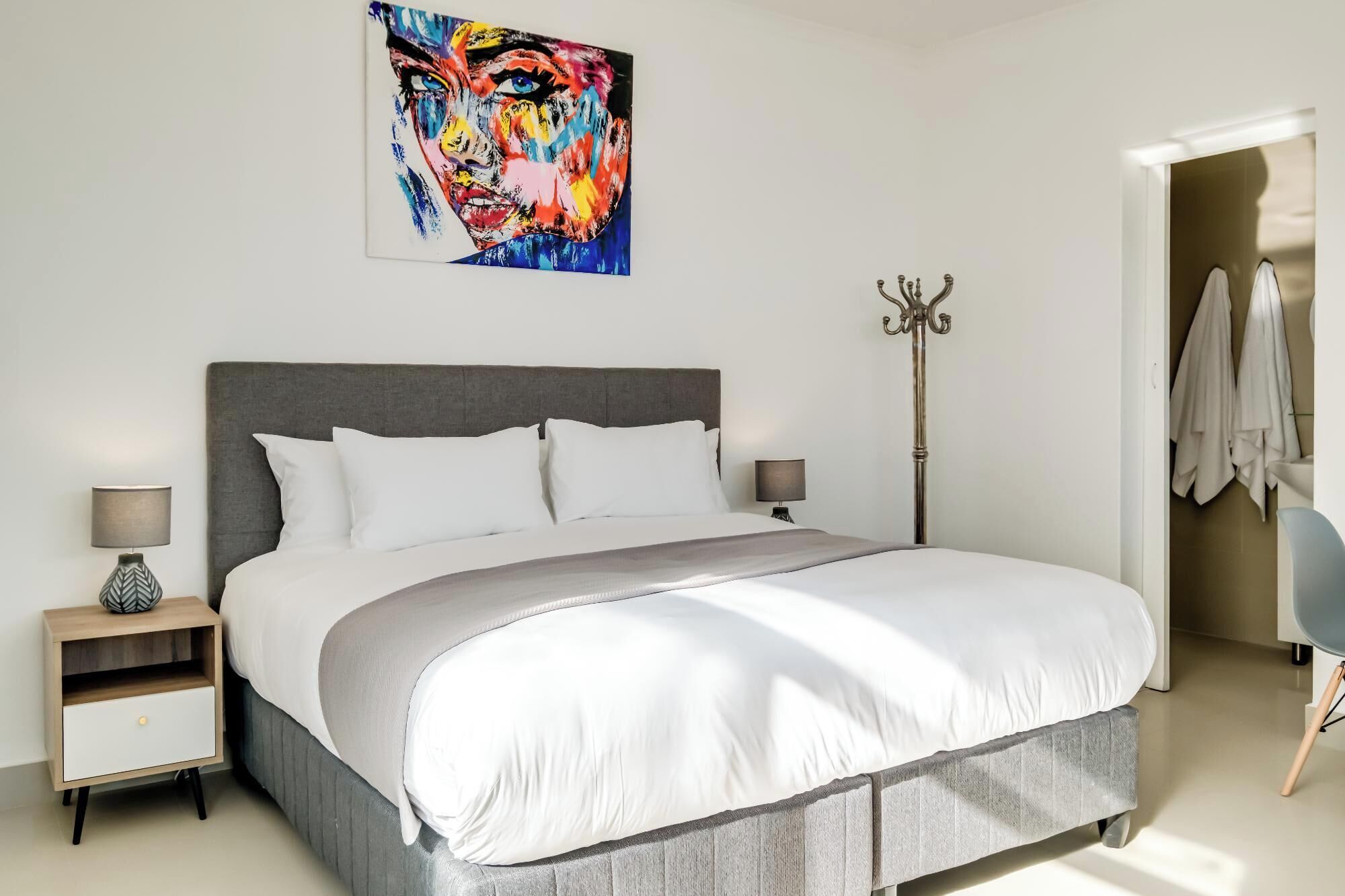 Ein modernes Schlafzimmer mit einem großen Bett, zwei Nachttischen, einer Stehlampe und einem Bild an der Wand.