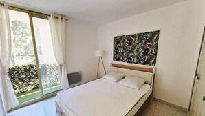 A bedroom with a bed, a window with curtains, a wall-mounted painting, and a floor lamp. - Swimming pool, Wi-Fi, private garage, terrace, walking distance to beaches and shops. (ST MANDRIER SUR MER)