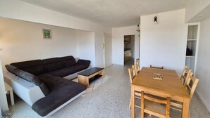 A living room with a dark-colored sofa, a wooden coffee table, and a dining table with chairs. There is a kitchen visible in the background. - Swimming pool, Wi-Fi, private garage, terrace, walking distance to beaches and shops. (ST MANDRIER SUR MER)