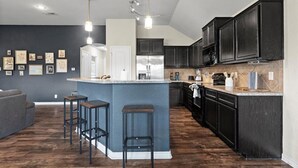 Een moderne keuken met donkere kastjes, een centraal eiland met krukken, hanglampen en kunst aan de muren.