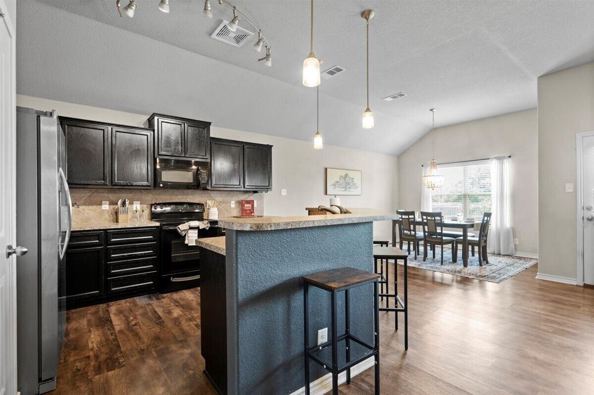 Une cuisine moderne avec des meubles de couleur sombre, un îlot central et des luminaires suspendus.