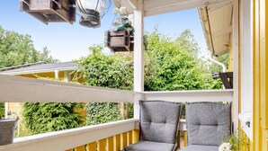 A balcony with yellow railings, two grey cushioned chairs, a small table with a vase of flowers, and hanging lanterns. - Kvarnfallet 40 by Interhome (Källsjö)