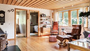A cozy room with wooden flooring, a fireplace, a bookshelf, and a window with a view of greenery. - Kvarnfallet 40 by Interhome (Källsjö)