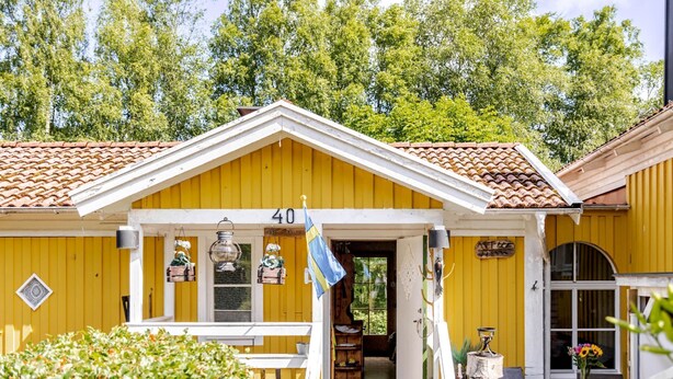 A yellow building with the number 40, a porch with potted plants, and a flag. - Kvarnfallet 40 by Interhome (Källsjö)