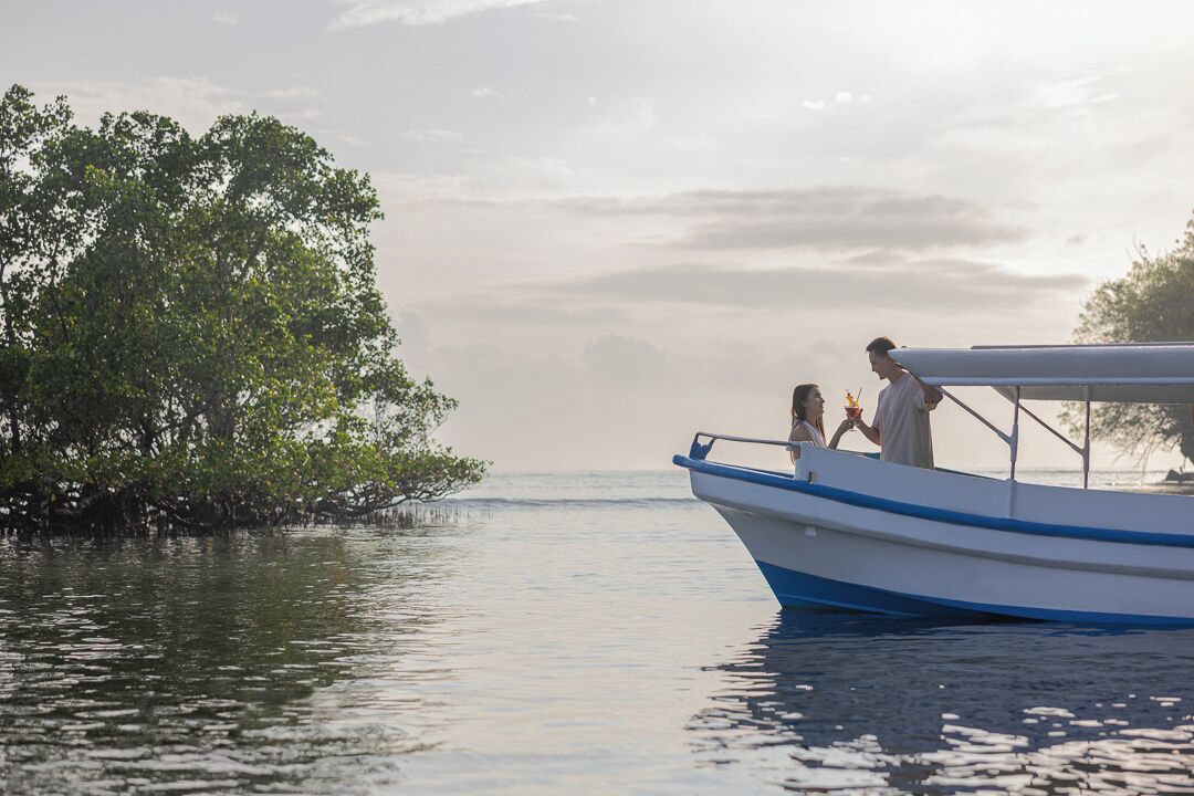 Un bateau avec une personne et un enfant à bord, entouré d’une eau calme et de mangroves.