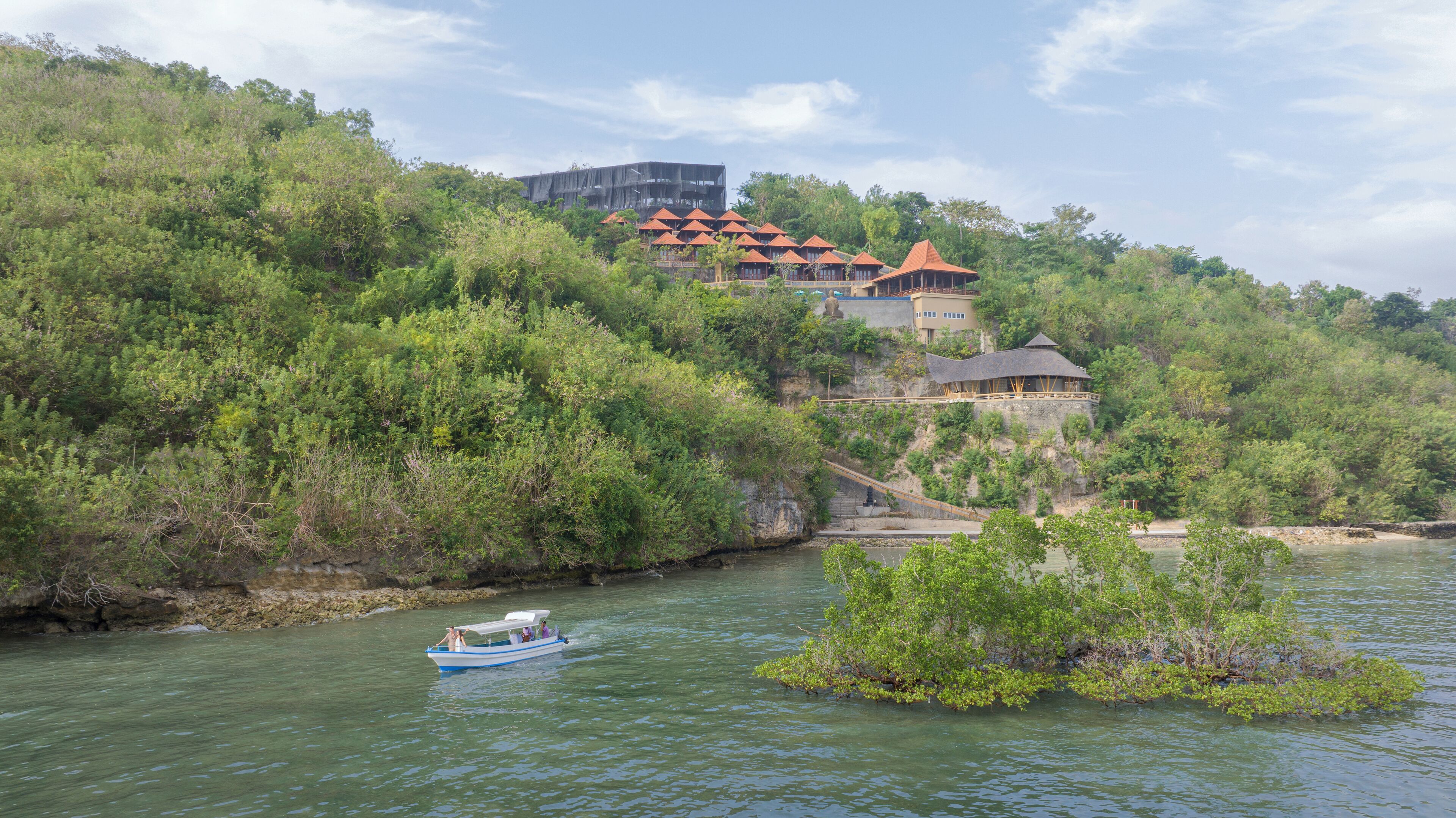 Un hotel a orillas del río con arquitectura tradicional, un bote en el agua y abundante vegetación.