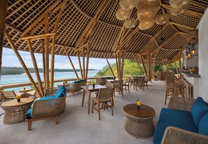 Een terras met rieten meubels, een bar en uitzicht op zee.