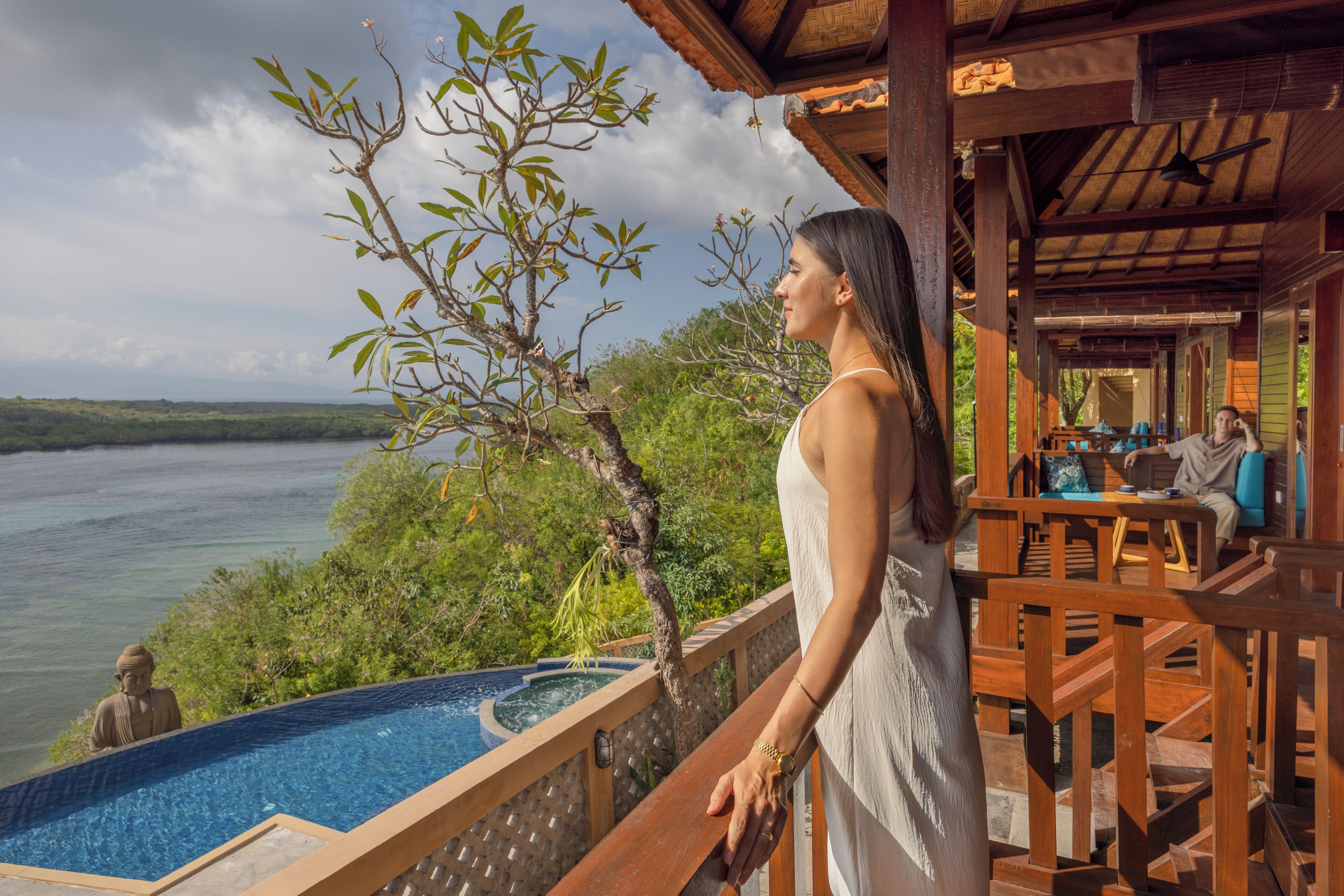 Una mujer de pie junto a una terraza de madera con vistas a una piscina y un río.