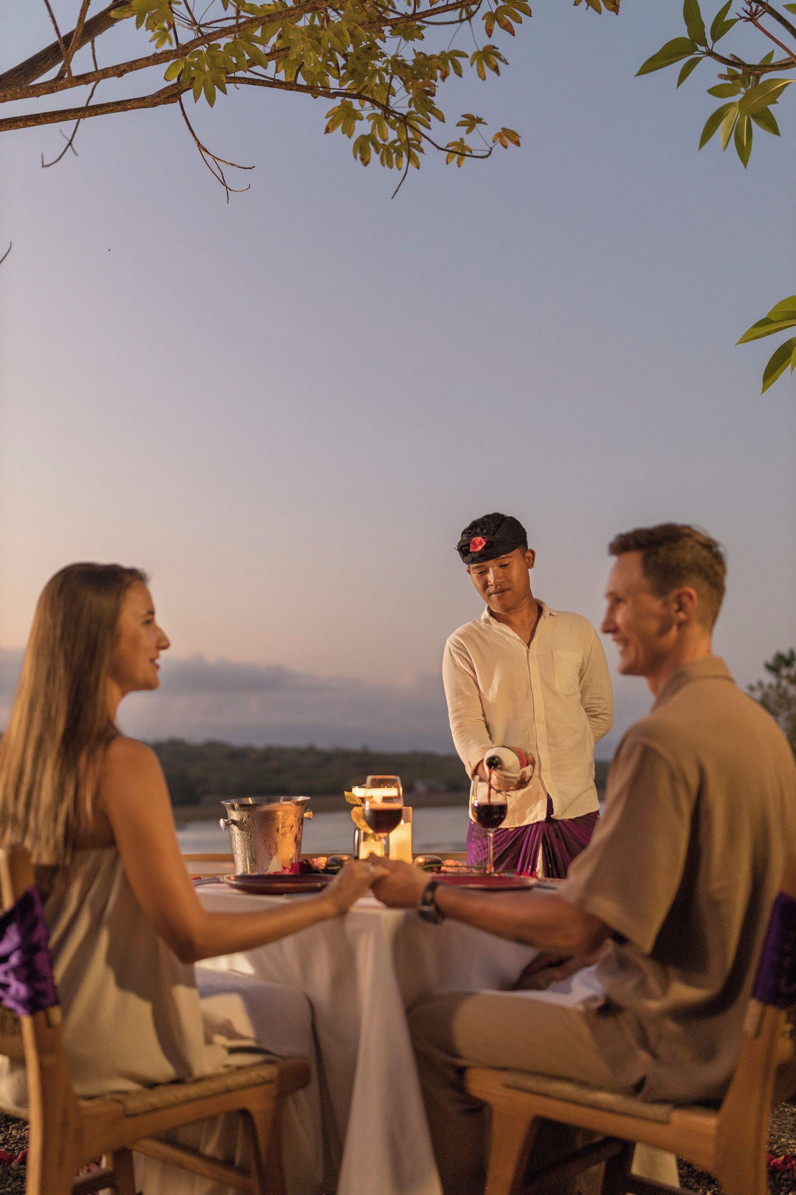Un grupo de personas cenando al aire libre en una mesa con vista al cielo y árboles.