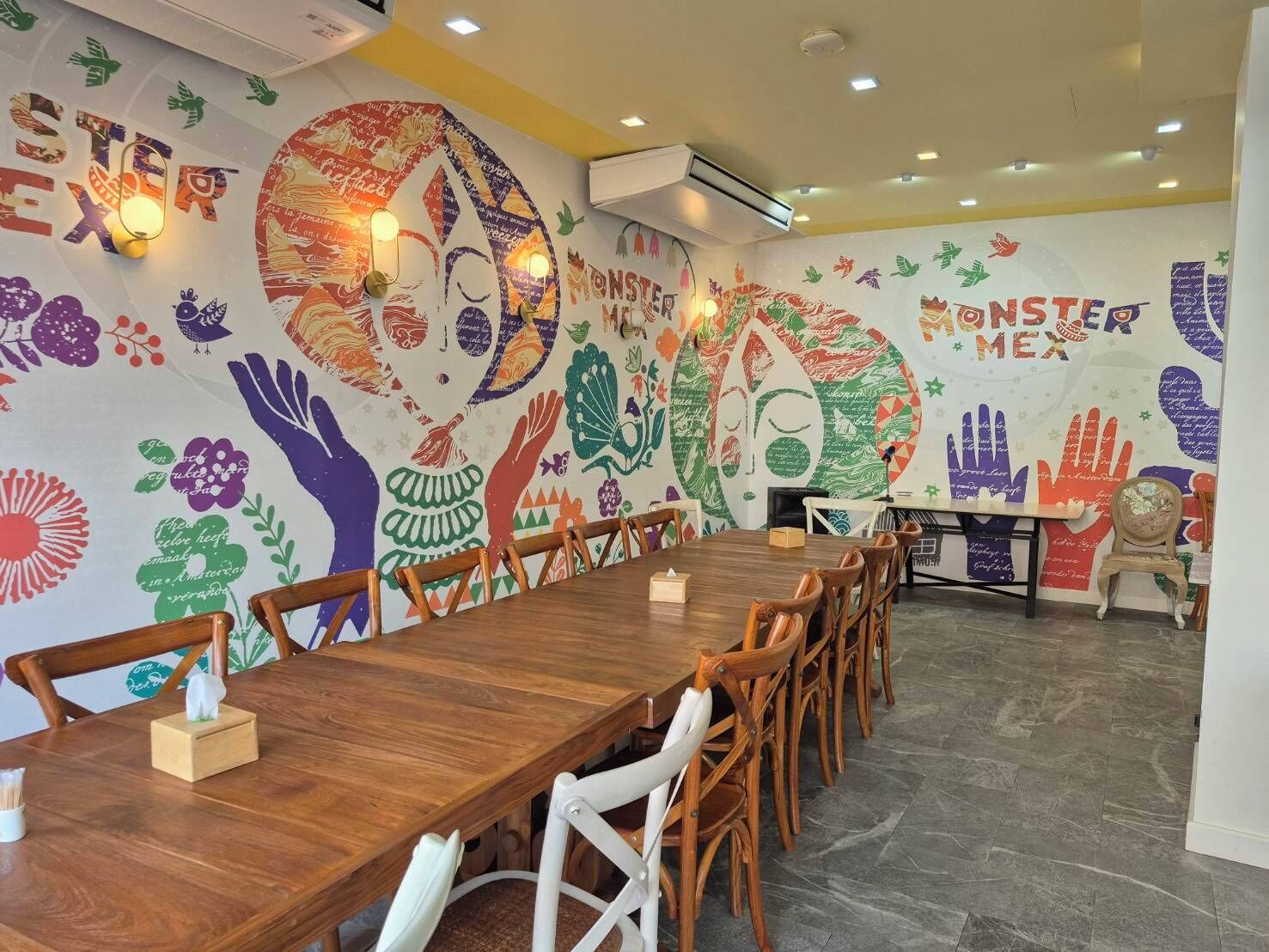 Un salón de conferencias con una larga mesa de madera, sillas blancas y coloridos murales en las paredes.