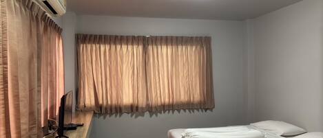 A bedroom with a bed, a window with curtains, a ceiling light, and an air conditioning unit.