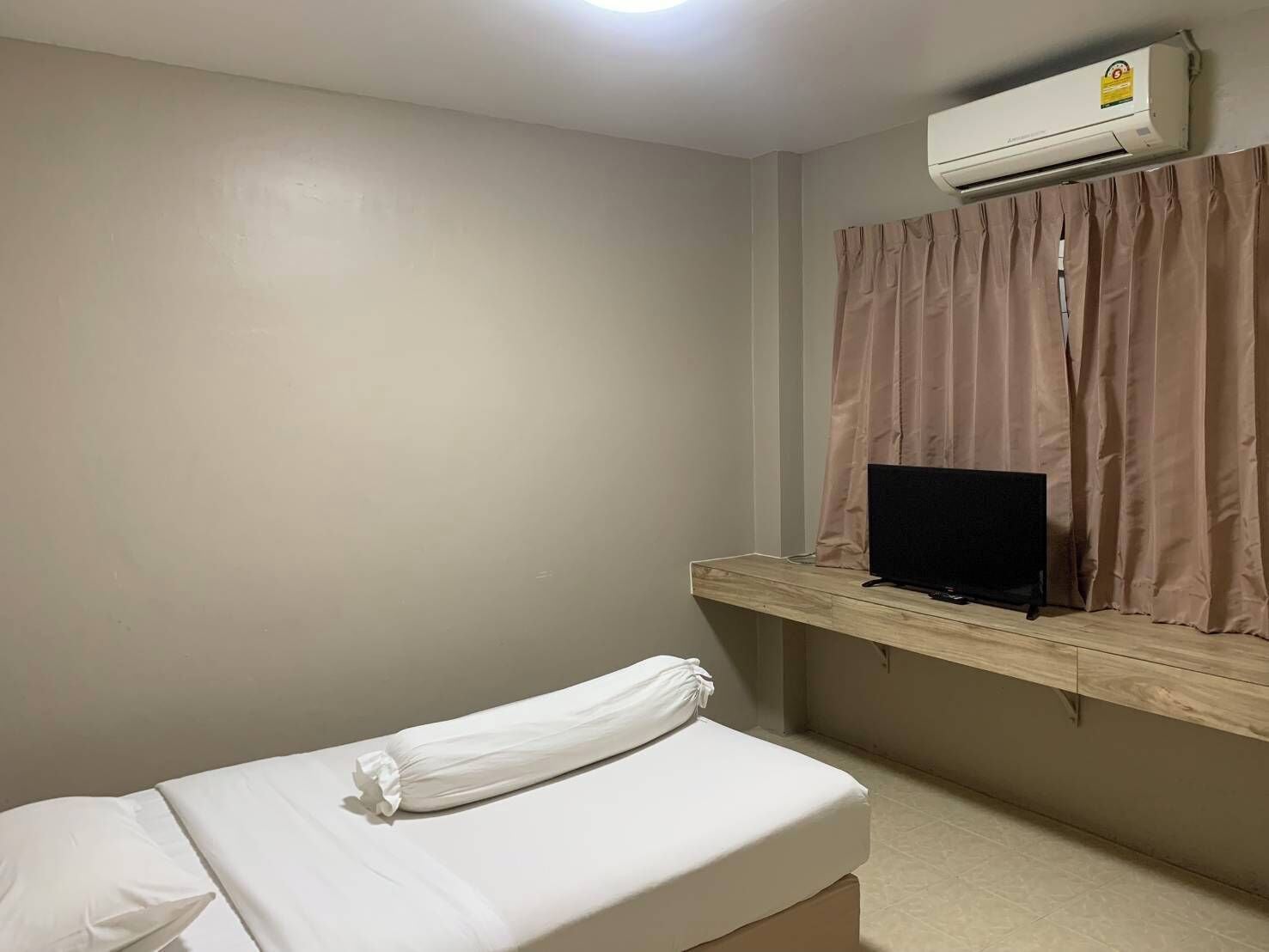 A hotel room with a bed, a TV on a wooden shelf, and an air conditioning unit.