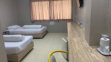 Habitación de hotel con dos camas, un escritorio de madera, una silla, un equipo de aire acondicionado y una ventana con cortinas.