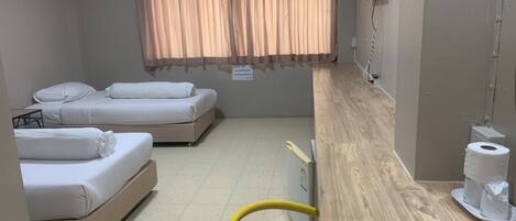Habitación de hotel con dos camas, un escritorio de madera, una silla, un equipo de aire acondicionado y una ventana con cortinas.