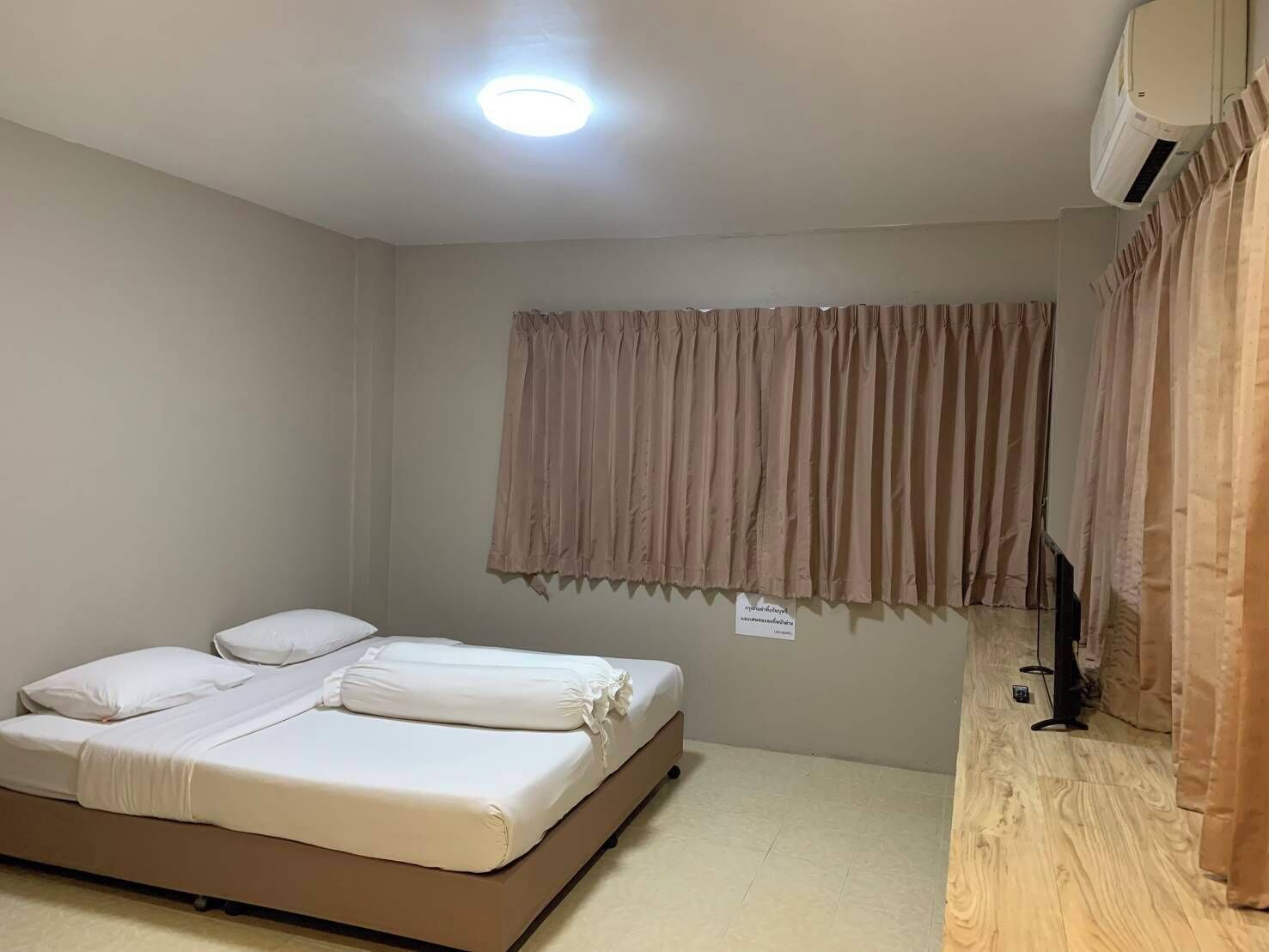 Una habitación pequeña con una cama individual, suelo de madera, una luz en el techo y una ventana con cortinas.