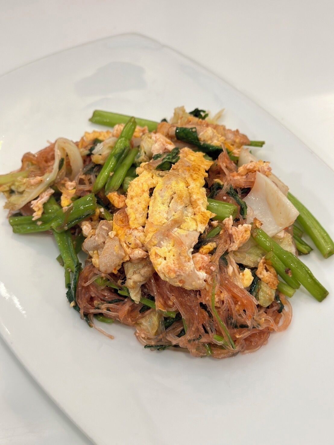 A dish with noodles, vegetables, and scrambled eggs on a white plate.