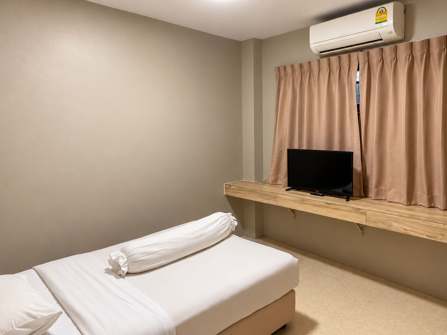 Habitación de hotel con cama, televisión sobre una repisa de madera y equipo de aire acondicionado.