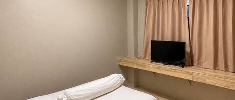 Habitación de hotel con cama, televisión sobre una repisa de madera y equipo de aire acondicionado.