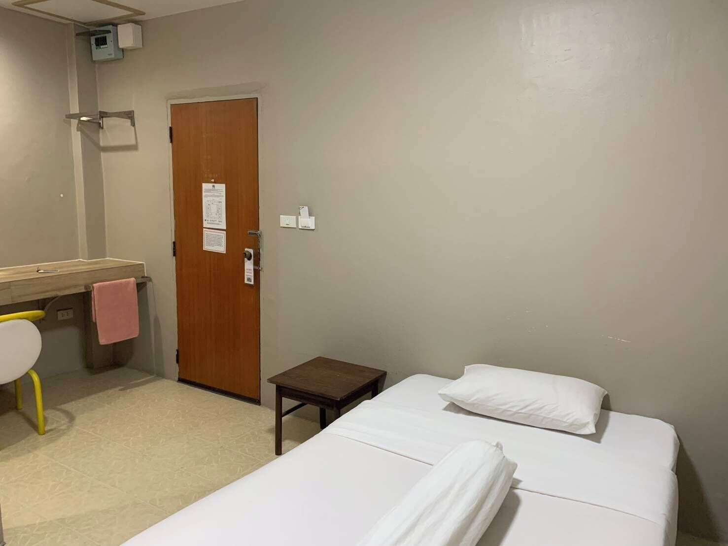 A hotel room with two single beds, a wooden door, a small table, a toilet, and a sink with a towel hanging on it.