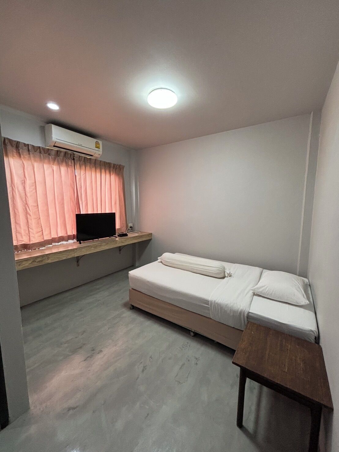 A small, tidy room with a single bed, a desk with a computer, and a window with curtains.