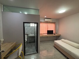Habitación pequeña con cama, escritorio con computadora, baño con baldosas estampadas y ventana con cortinas.