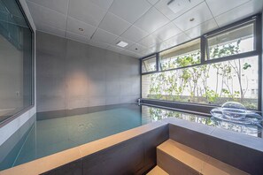 A modern indoor swimming pool with a glass wall and a view of greenery outside. - Busan Gwangalli The Moor Hotel (Busan)