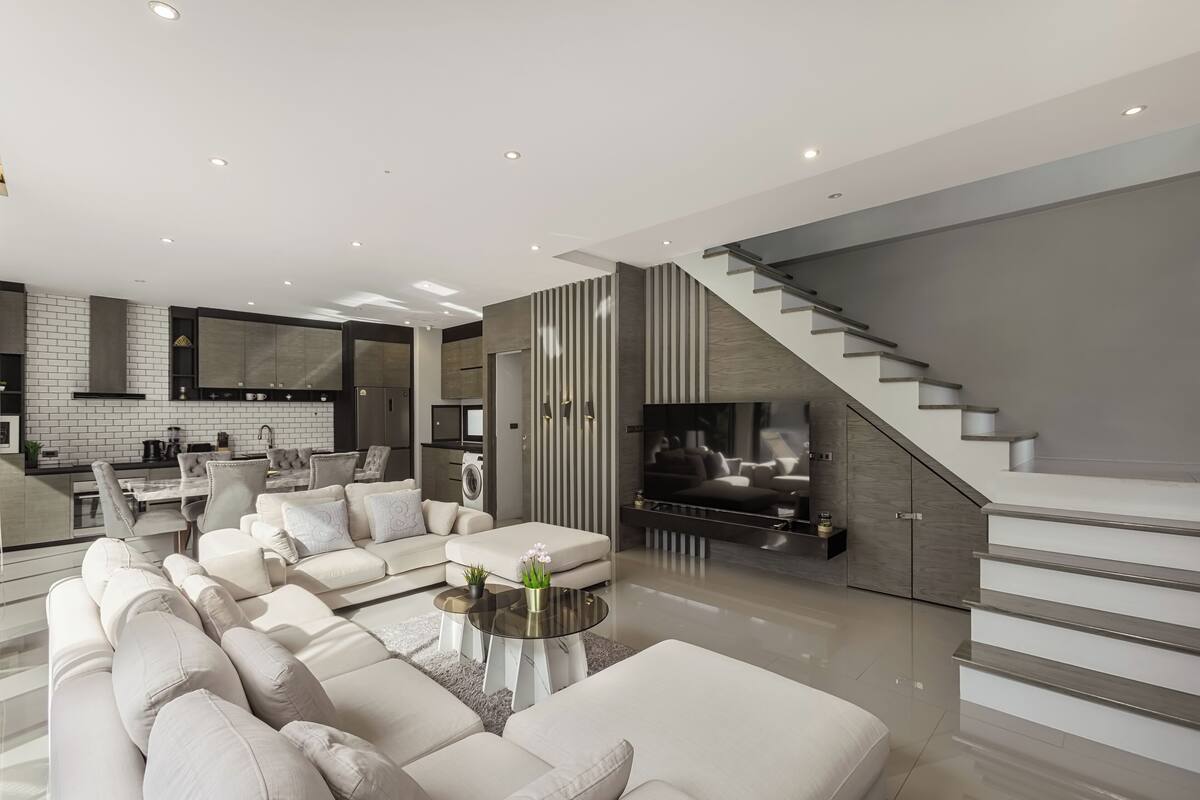 A modern living room with a large sectional sofa, a coffee table, and a TV. There is a staircase leading to an upper level.
