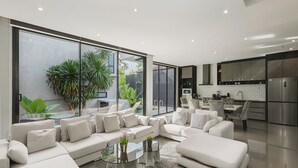 Ein modernes Wohnzimmer mit einem großen Ecksofa, einem Glastisch und Blick auf den Garten.