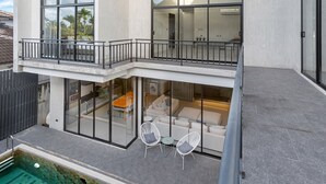 Ein modernes, zweistöckiges Haus mit Balkon, Schwimmbad und einer Terrasse mit Gartenmöbeln.