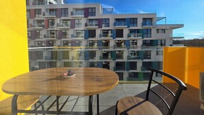 Un balcone con un tavolo rotondo in legno e una sedia, con vista su un moderno edificio a più piani con balconi.