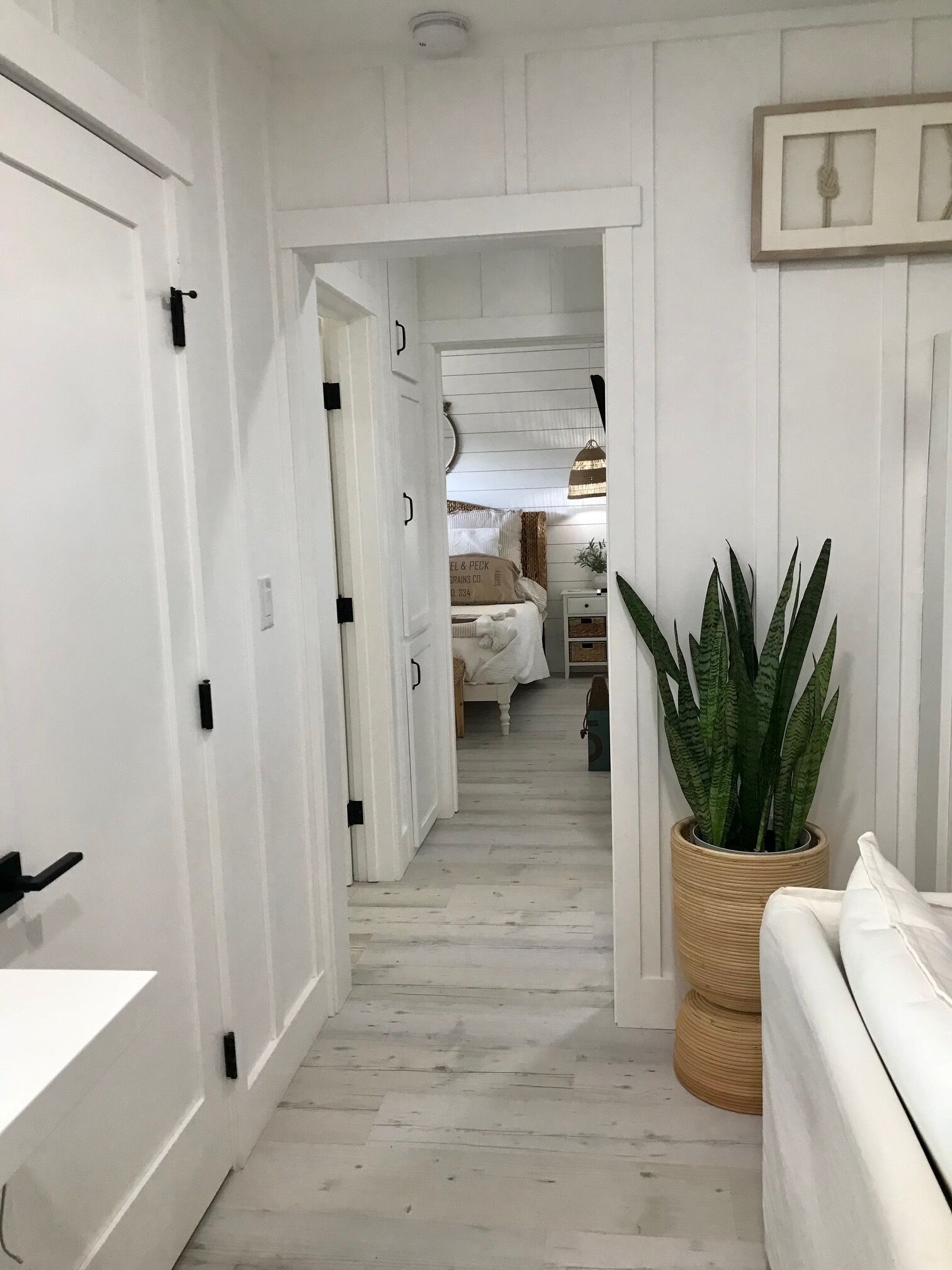 A hallway with white walls and wooden flooring leading to a bedroom.