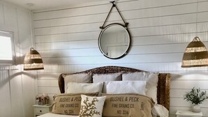 Une chambre à coucher avec un lit, des tables de chevet, un miroir suspendu et un ventilateur de plafond.