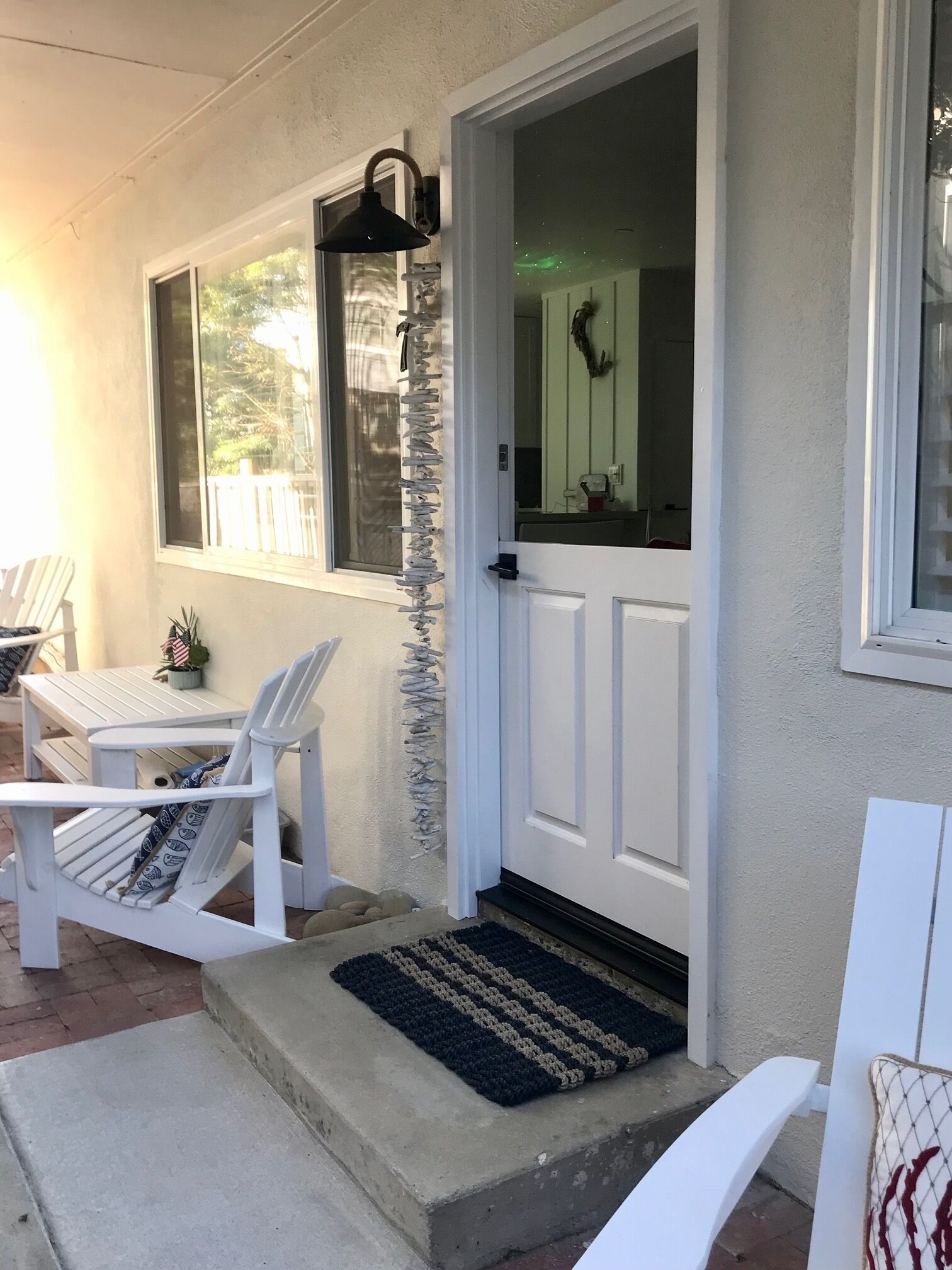 En veranda med hvide stole, et lille bord og en dør med dørmåtte.