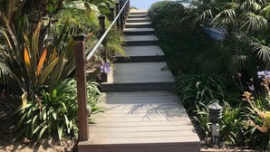 Un escalier menant à un bâtiment, entouré d’une végétation luxuriante et bordé d’un chemin en briques.