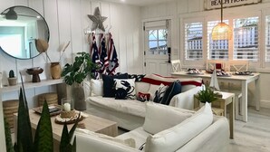 Un salon avec un canapé blanc, une table à manger avec des chaises, un ventilateur de plafond et une pancarte sur laquelle on peut lire « MAISON DE PLAGE ».