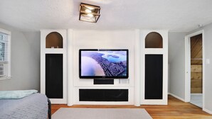 Un salon moderne avec un téléviseur à écran plat fixé à un mur blanc, encadré par des haut-parleurs noirs, un parquet en bois et un tapis gris.