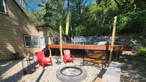 Un jardin avec un foyer, des fauteuils Adirondack rouges, un banc en bois et une table avec des chaises.