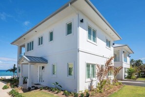 A two-story white house with green shutters, a covered porch, and a view of the ocean. - Oceans 9 LUXE | 4BR Beachfront Villa in West Bay (West Bay)