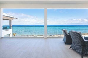 A balcony with a view of the ocean, two wicker chairs, and a small table. - Oceans 9 LUXE | 4BR Beachfront Villa in West Bay (West Bay)