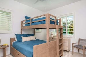 Un lit superposé avec une structure en bois, un matelas bleu et des oreillers assortis. Il y a une petite table de chevet avec une lampe, une chaise et une fenêtre avec des stores.