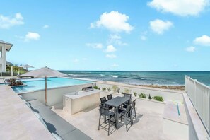 Una piscina en la azotea con vistas al océano, zona de barbacoa y mobiliario de exterior.