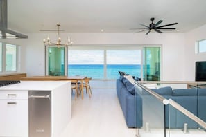 Ein modernes Wohnzimmer mit einem großen Glasfenster, das auf einen Balkon mit Blick auf das Meer führt.