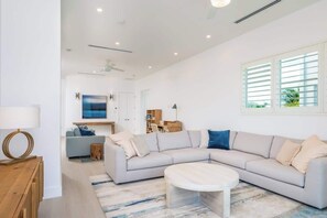 Ein modernes Wohnzimmer mit einem großen, L-förmigen Ecksofa, einem runden Couchtisch und einem Essbereich im Hintergrund.